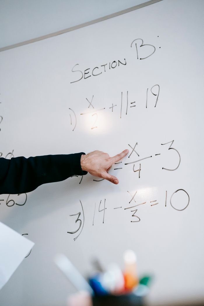Close-up of an instructors hand solving math equations on a whiteboard during a lesson.